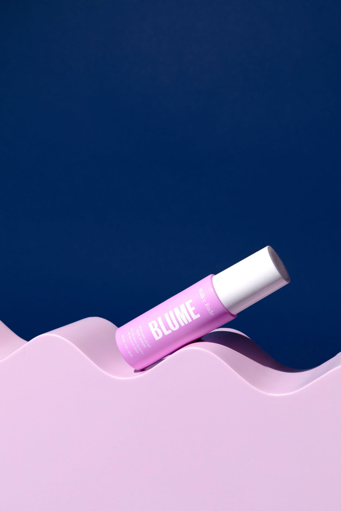Blume skincare Milky Fade Serum flat lay on wavy pink surface with dark blue background, clean beauty branding.