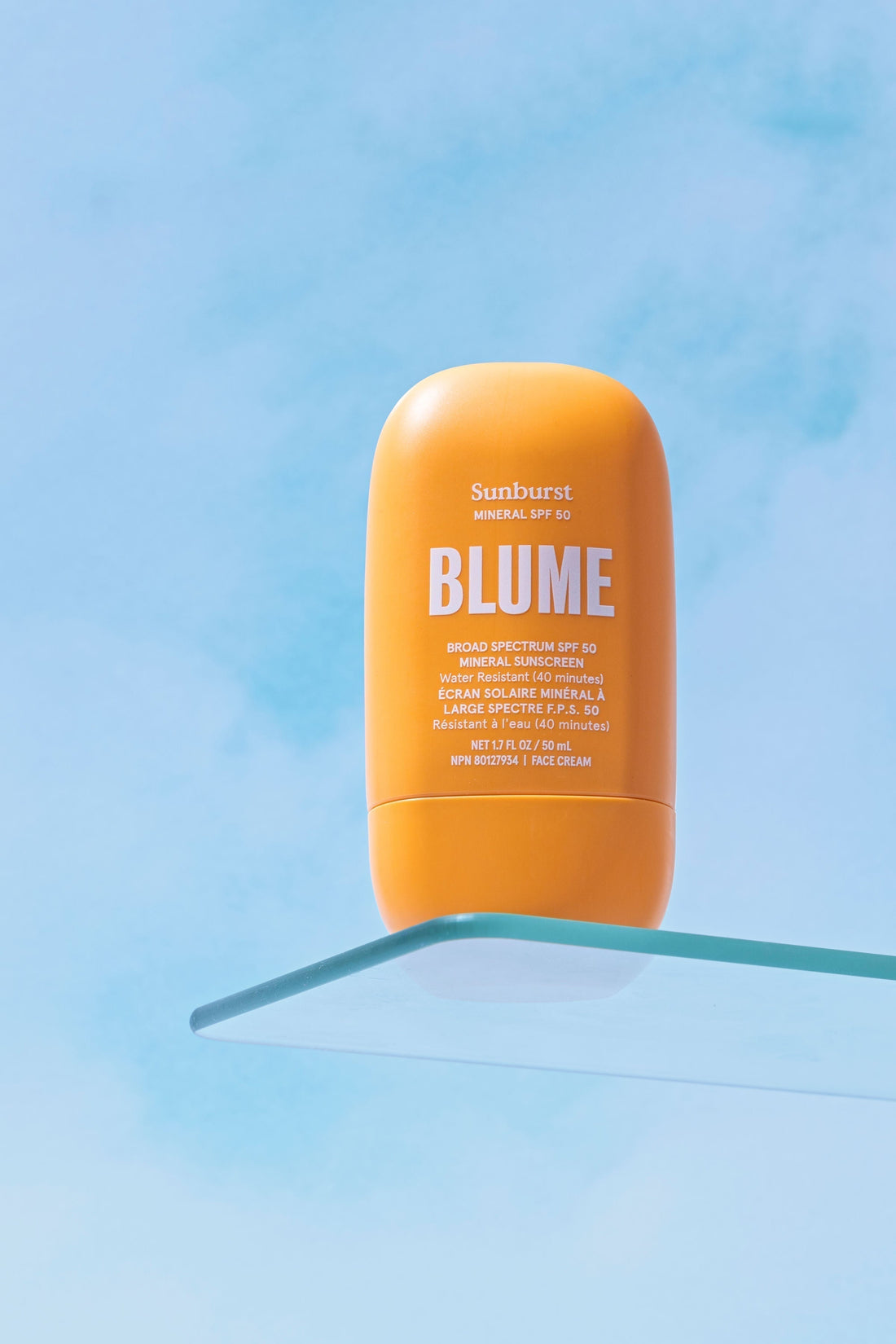 Blume Sunburst Mineral SPF 50 sunscreen on glass shelf with sky background
