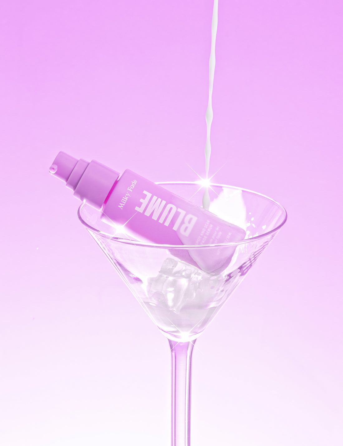 Blume Milky Fade Serum in a martini glass with ice, styled against a pink background with milk pouring in, representing hydration and brightness for skin.