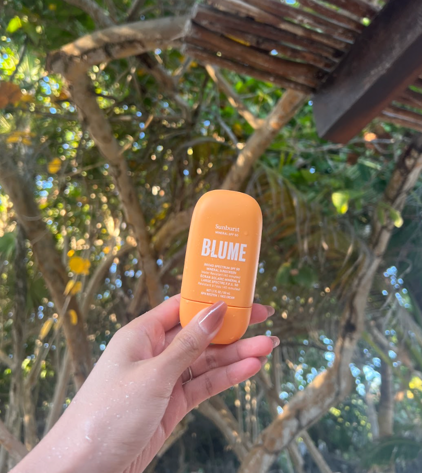 Blume Sunburst Mineral SPF 30 sunscreen held in hand outdoors under tropical trees, showcasing eco-friendly, travel-size sun protection in natural sunlight