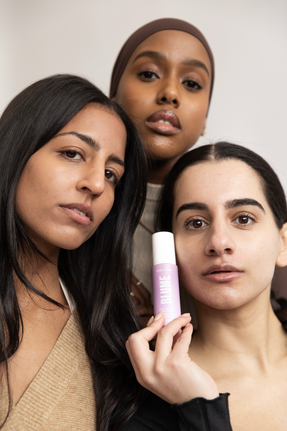 Three women with natural skin holding Blume Milky Fade Serum, showcasing skincare diversity