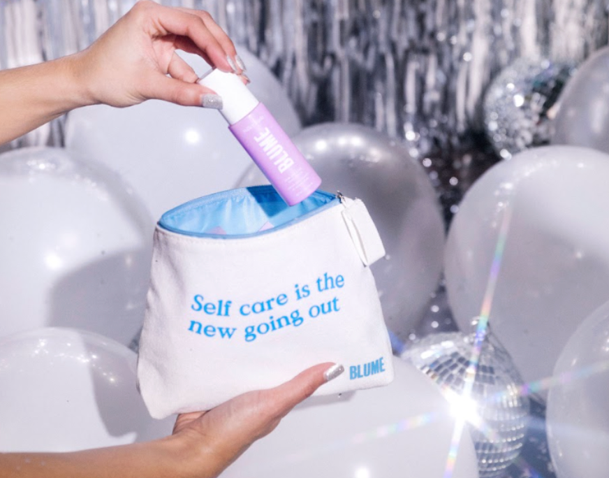 Hand placing a Blume skincare bottle into a pouch that says “Self care is the new going out,” surrounded by balloons and disco balls.