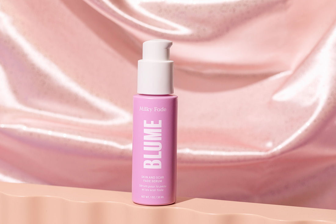 Blume Milky Fade Skin and Scar Fade Serum in pink bottle on a soft pink satin background – dark spot and scar treatment skincare product.
